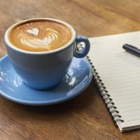 Cup of coffee and pen and notebook on wood desk