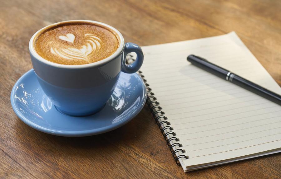 Cup of coffee and pen and notebook on wood desk