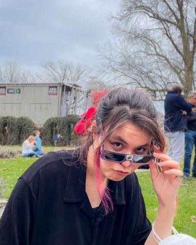 Asian women peeking over sunglasses in outdoor garden setting.